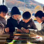 ガラス工房でとんぼ玉の素材を選ぶ子どもたちの様子。色とりどりのガラス棒を前に真剣に選んでいる。